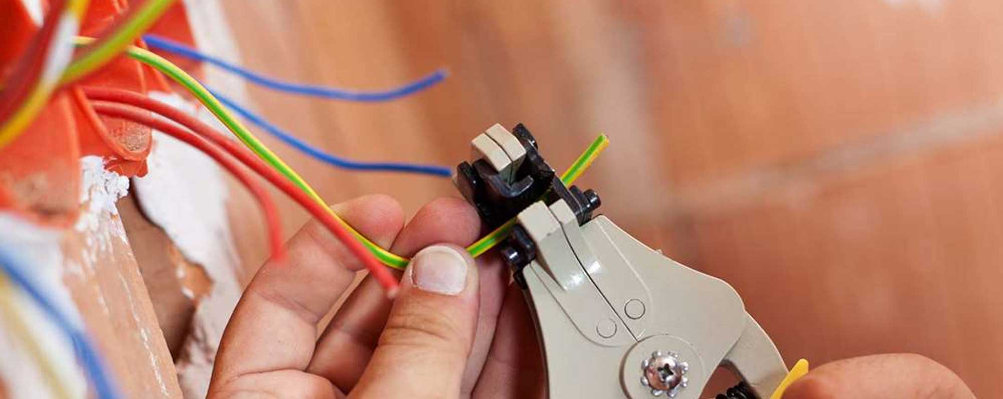 Electrician using wire strippers to strip insulation from colored electrical wires during installation