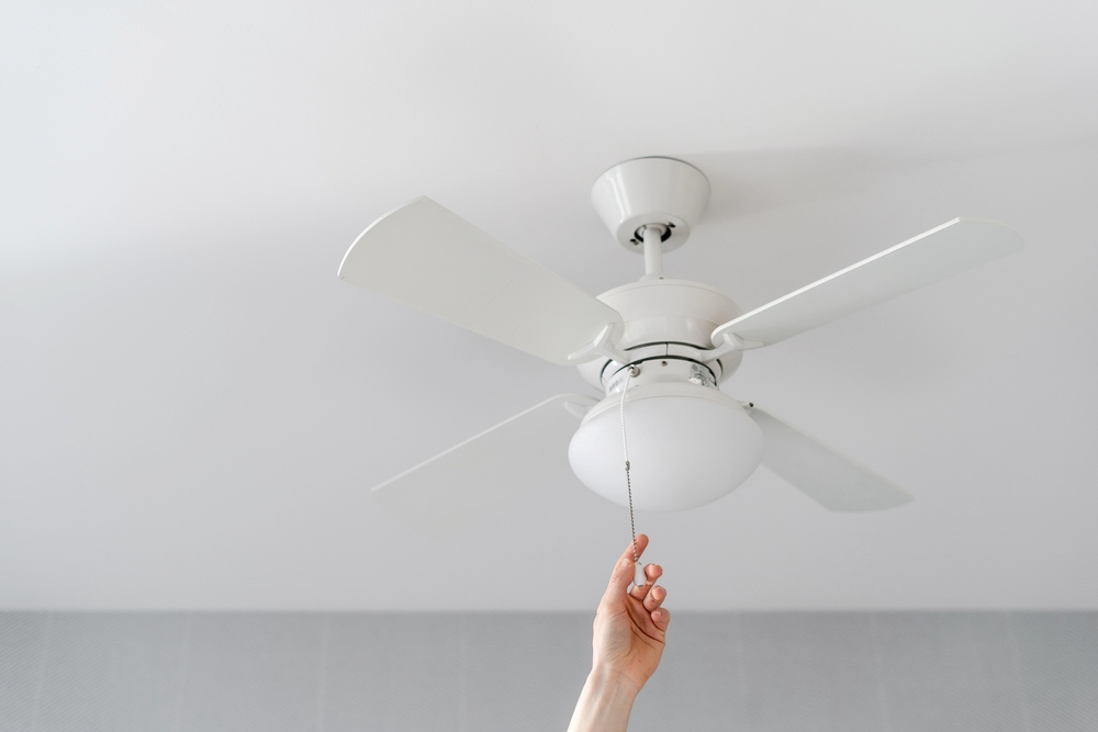 Image of a cropped shot of a female hand pulling the switch of a ceiling fan, featuring Anderson Lighting and Electric and highlighting professional ceiling fan installation services.
